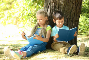 Zwei Kinder lehnen sitzend an einem Baum und halten jeweils ein Buch © AdobeStock_174500434/Africa Studio