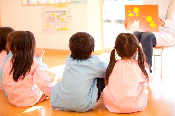 Kinderbetreuung, Kinder sitzen vor einer Betreuering, die ein Bild zeigt. © AdobeStock Paylessimages